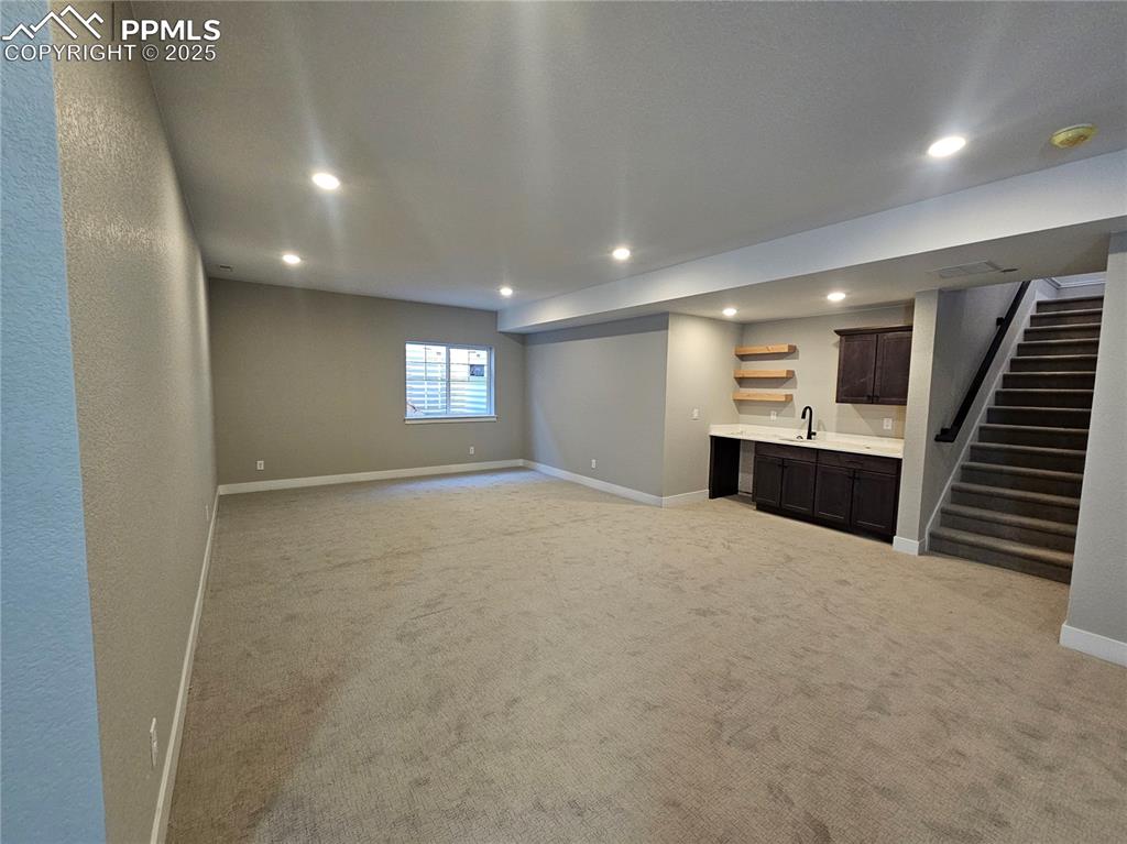 Image 9 of 12: Basement with recessed lighting, light colored carpet, stairway, and bar wi