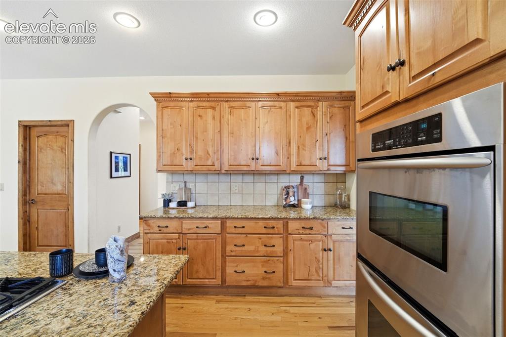 Image 7 of 50: Kitchen featuring wood cabinetry, light-toned granite countertops, stainles