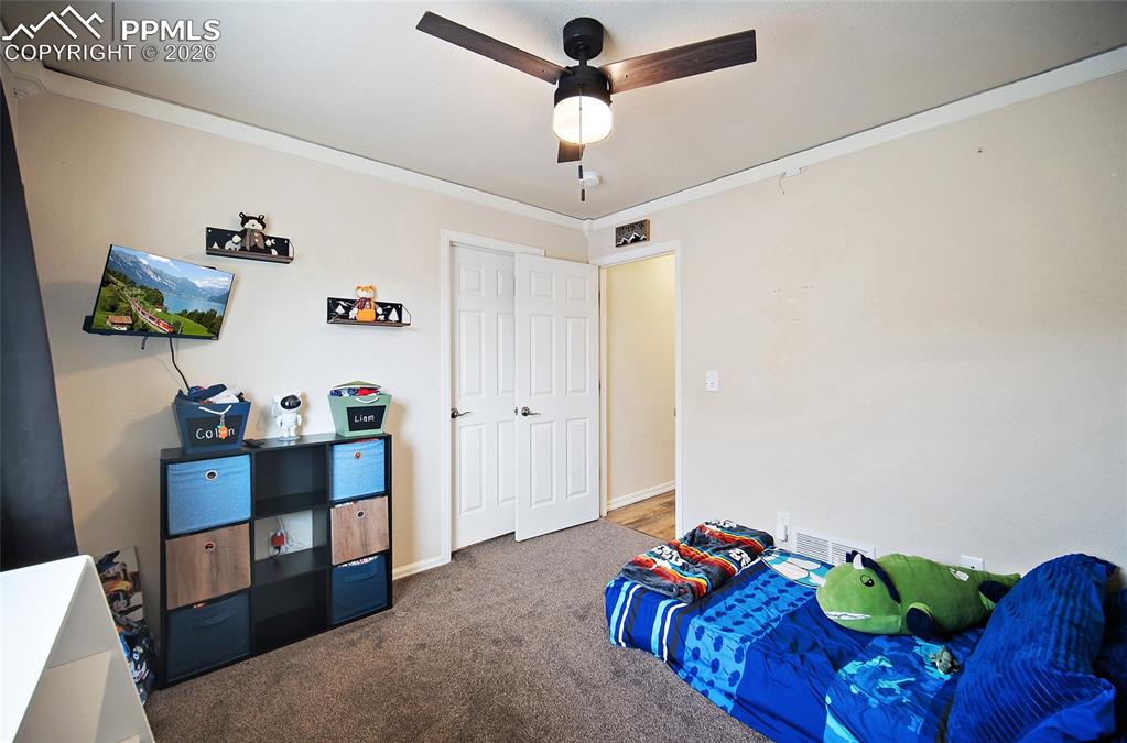 Image 21 of 43: Carpeted room with a ceiling fan light fixture, crown molding, and white ba