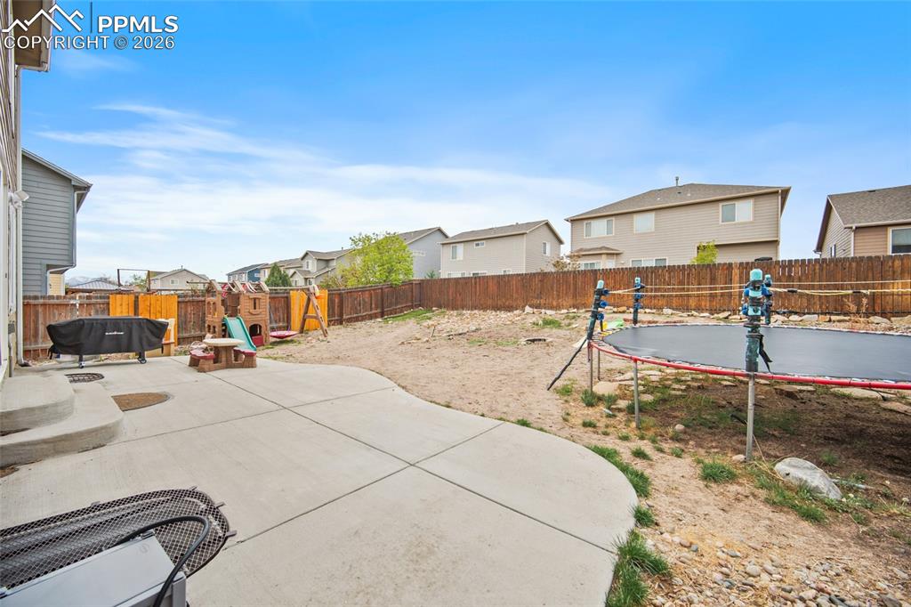 Image 27 of 43: Expansive backyard featuring a concrete patio, wood fencing, and a gravel a