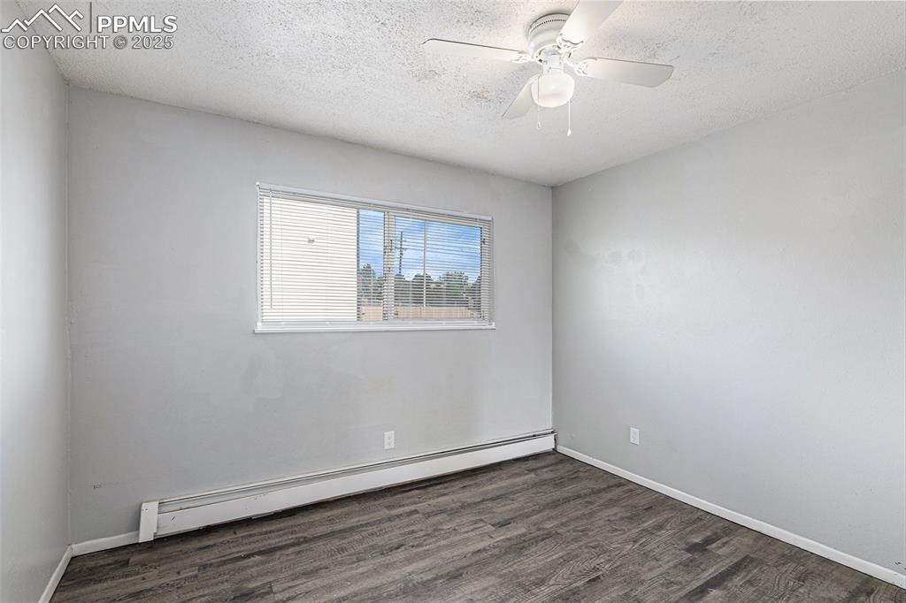 Image 11 of 18: Empty room with a baseboard radiator, a textured ceiling, wood finished flo
