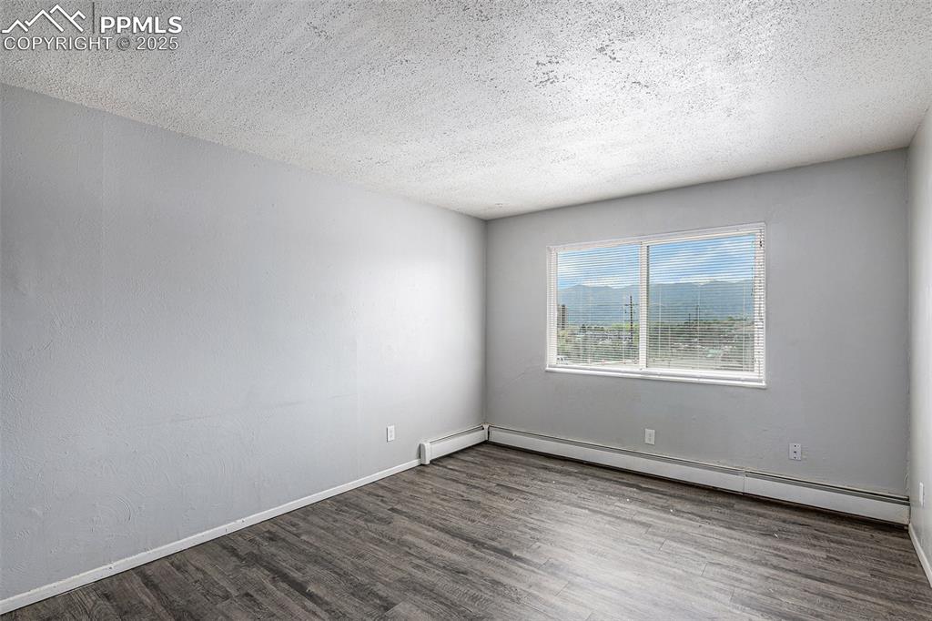 Image 4 of 18: Empty room with a textured ceiling, wood finished floors, and a baseboard h