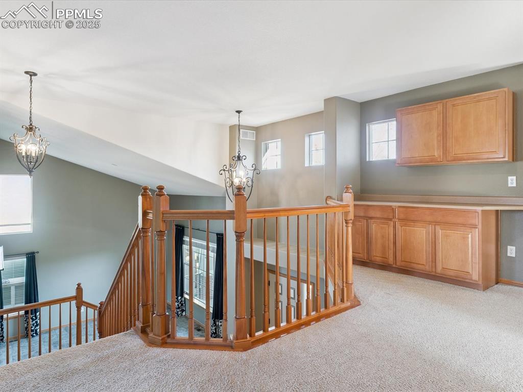 Image 27 of 45: Hallway with a chandelier, an upstairs landing, and light carpet
