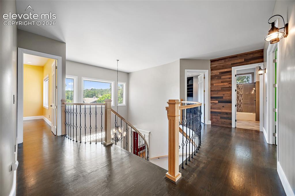 Image 28 of 50: Upper-level hallway featuring dark wood-finish flooring, a wood accent wall