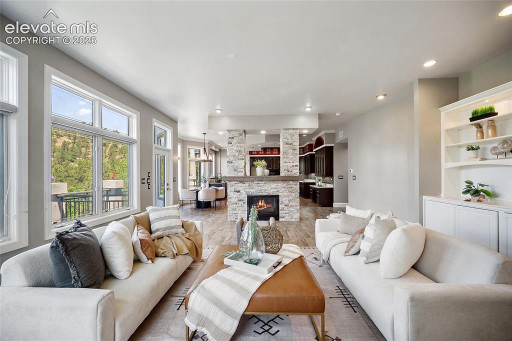 Image 8 of 50: Spacious living area featuring a stacked stone fireplace, large windows, wo