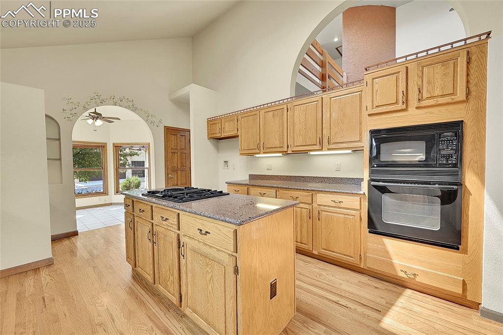 Image 10 of 30: Kitchen featuring high vaulted ceiling, black appliances, light stone count