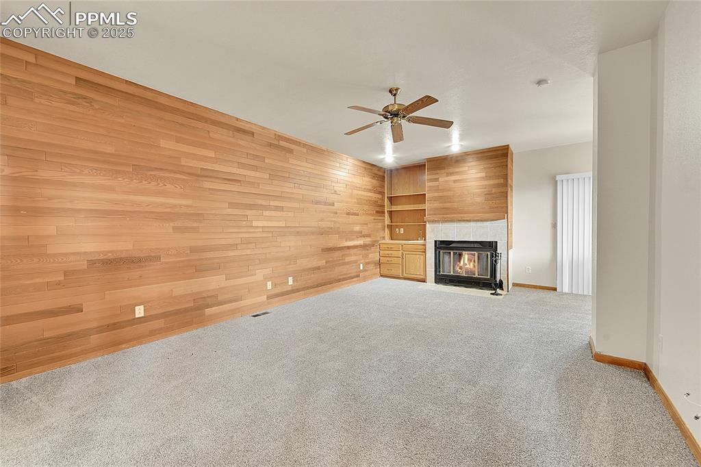 Image 22 of 30: Unfurnished living room with carpet floors, wood walls, a fireplace, a ceil