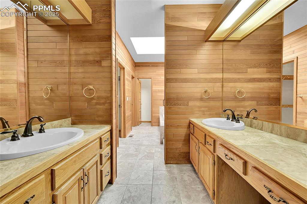 Image 25 of 30: Bathroom featuring wooden walls, two vanities, a skylight, and light tile p
