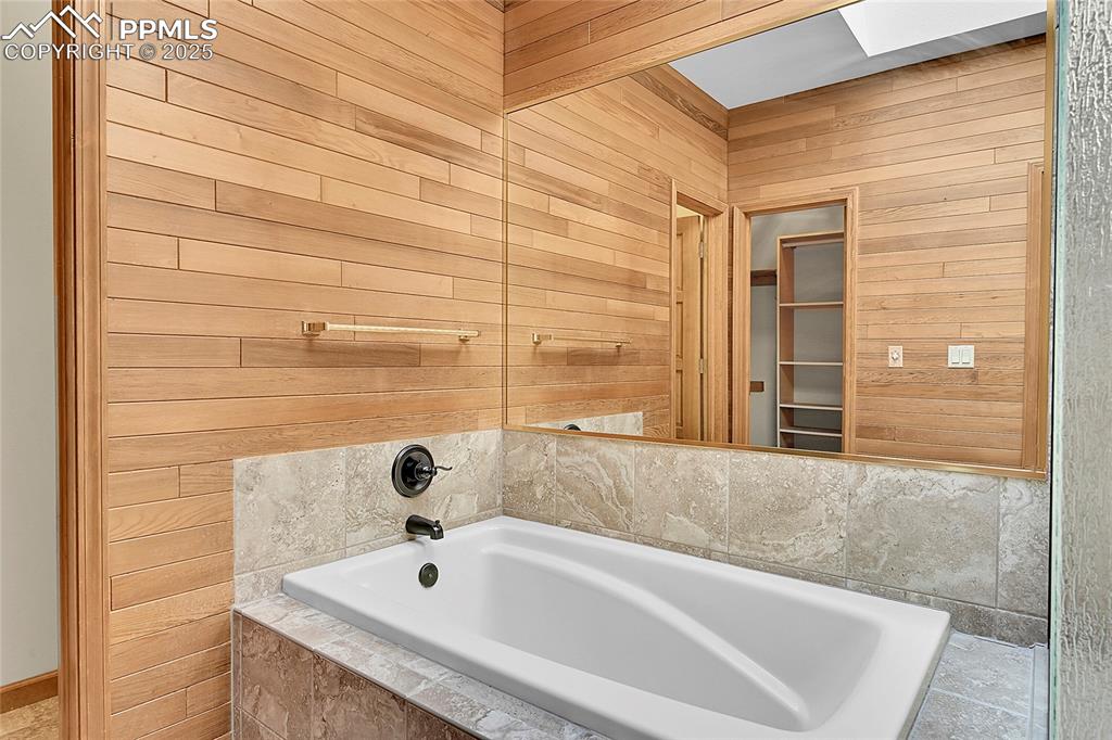 Image 26 of 30: Full bath with wood walls, a garden tub, and a skylight