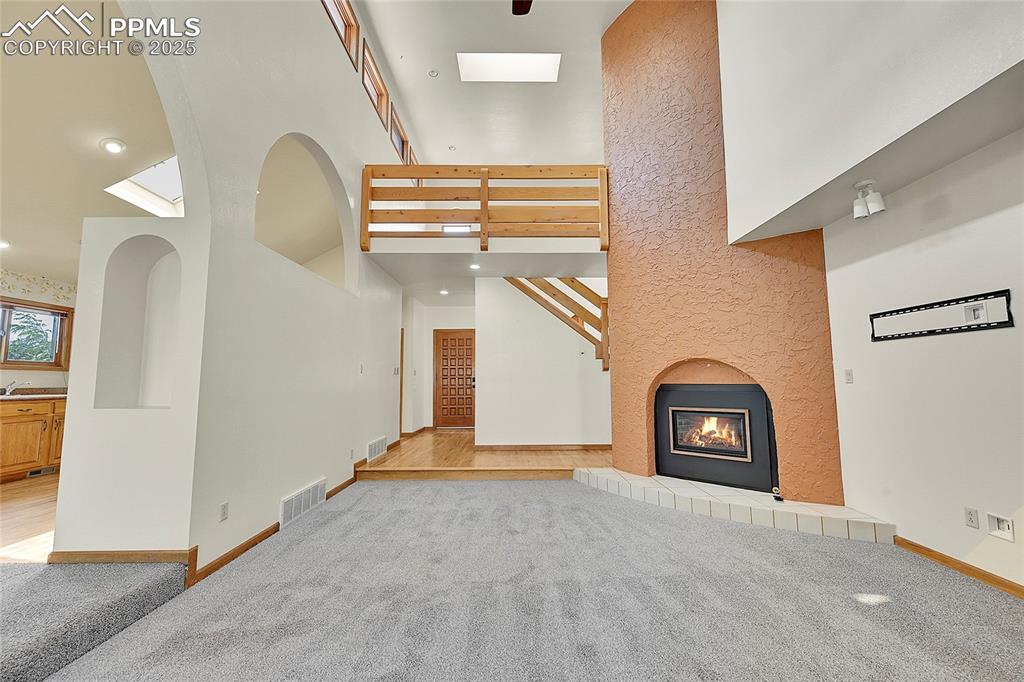 Image 3 of 30: Unfurnished living room featuring light carpet, a towering ceiling, a tiled