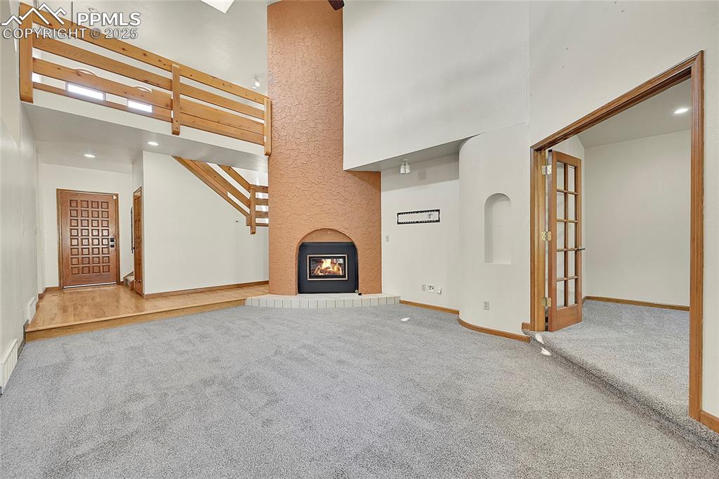 Image 8 of 30: Unfurnished living room featuring a towering ceiling, a glass covered firep