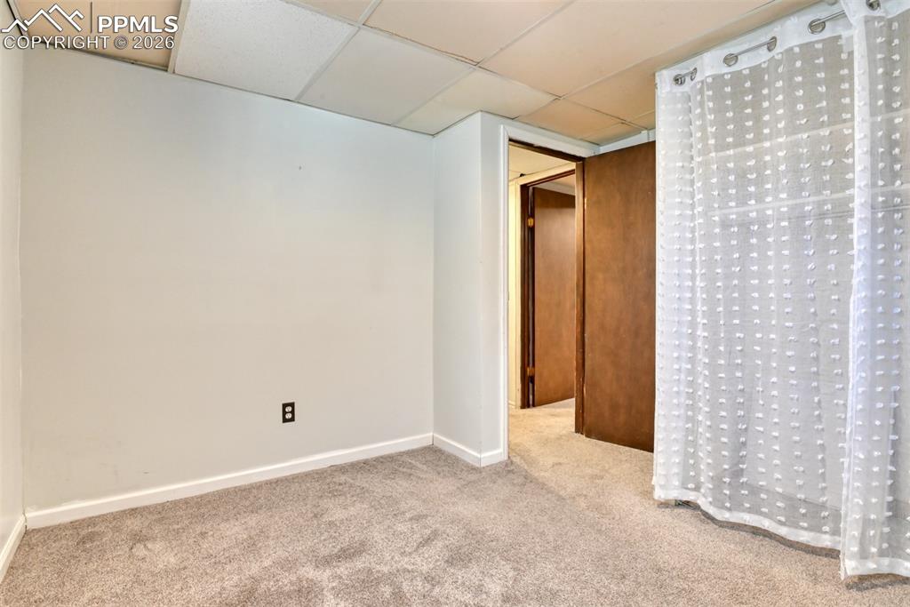 Image 24 of 47: Carpeted primary basement bedroom with a paneled ceiling and baseboards