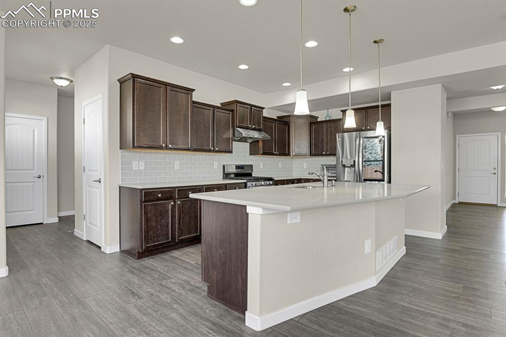 Image 10 of 31: Kitchen featuring dark brown cabinets, decorative backsplash, pendant light