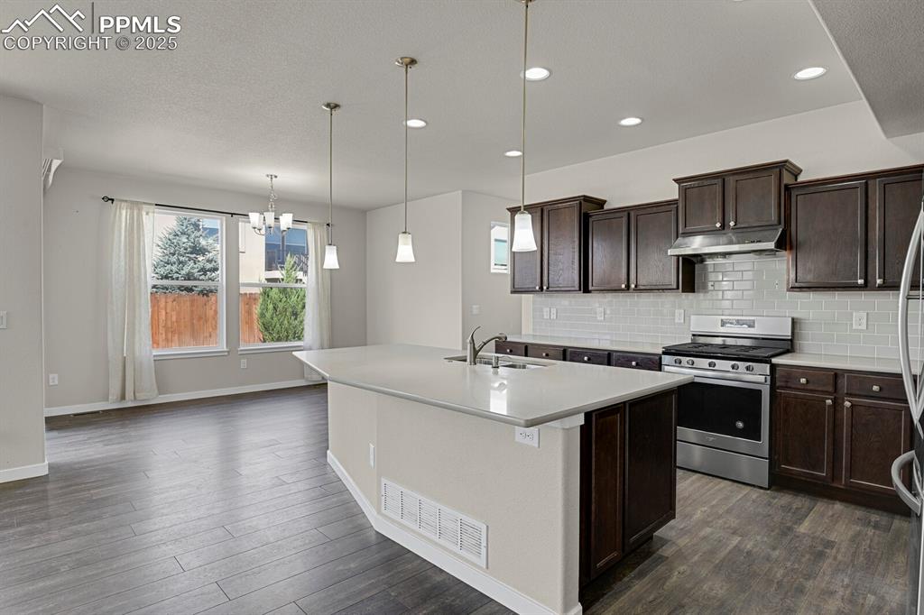 Image 11 of 31: Kitchen featuring stainless steel appliances, dark brown cabinetry, decorat