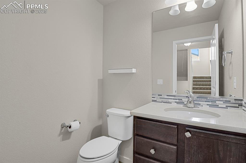 Image 13 of 31: Half bath with a textured wall, vanity, and decorative backsplash