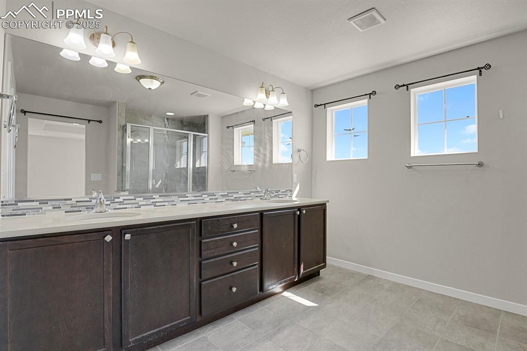 Image 18 of 31: Full bath featuring double vanity, a stall shower, and decorative backsplas