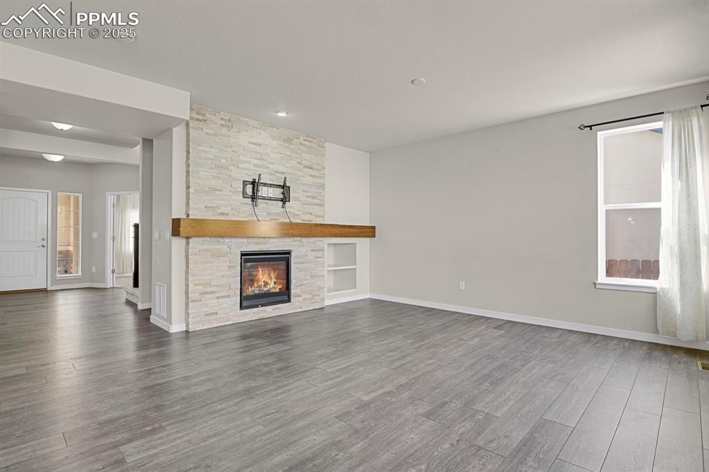 Image 8 of 31: Unfurnished living room featuring wood finished floors and a stone fireplac