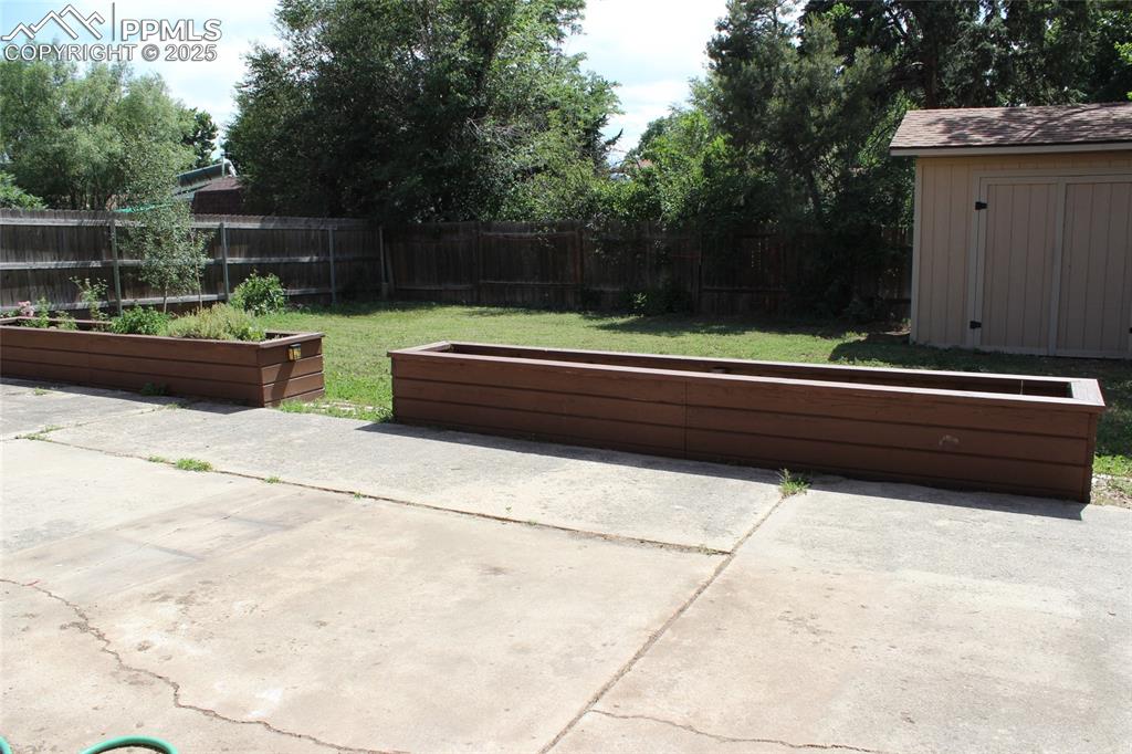 Image 25 of 25: Fenced backyard with a vegetable garden and a storage shed