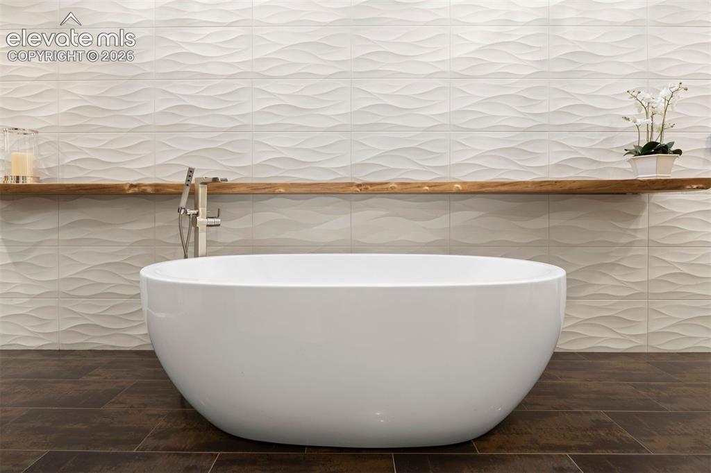 Image 17 of 36: Freestanding bathtub, with hand-held faucet, and wavy tile feature wall wit