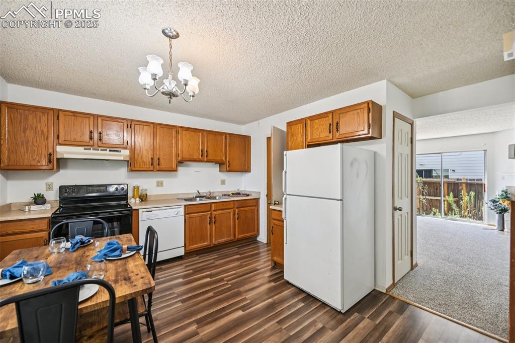 Image 10 of 28: Kitchen with white appliances, brown cabinetry, decorative light fixtures,