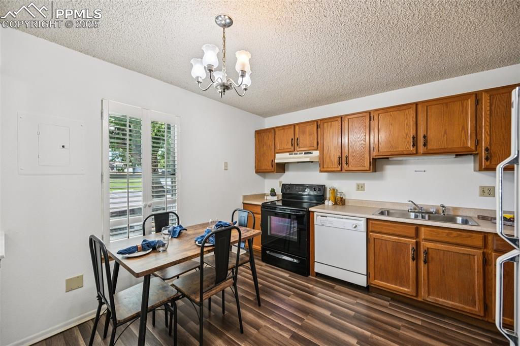 Image 11 of 28: Kitchen with white appliances, decorative light fixtures, brown cabinets, l