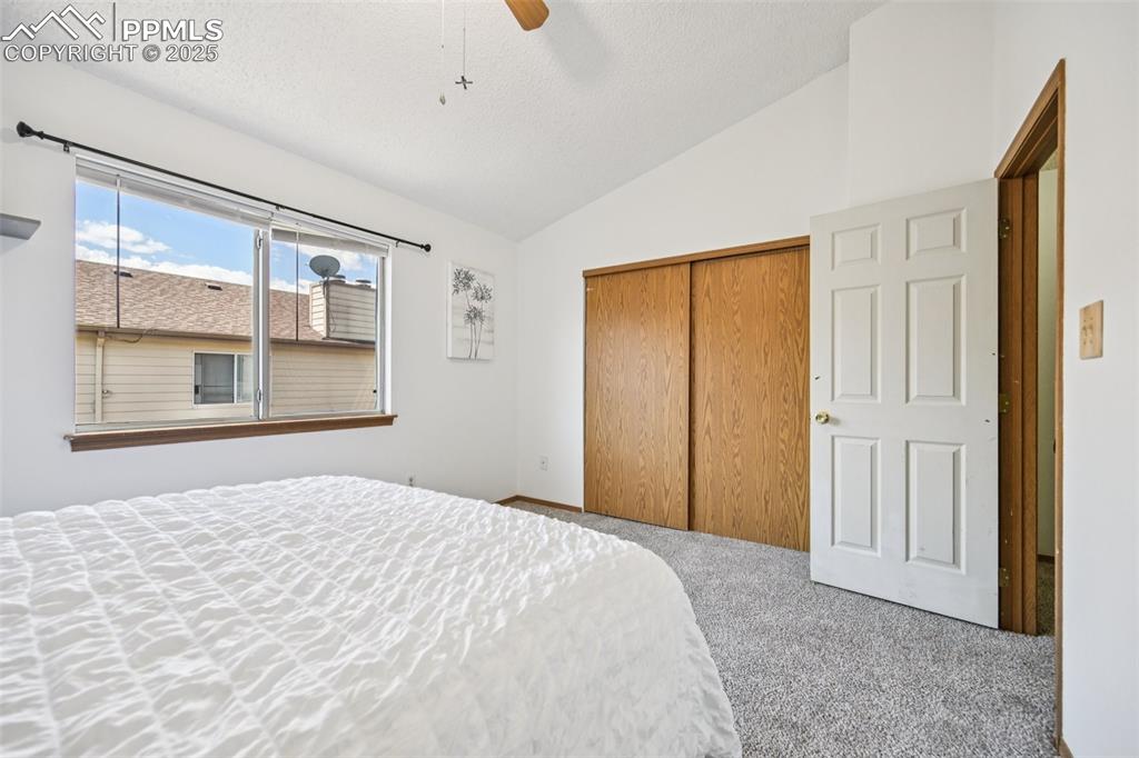 Image 19 of 28: Carpeted bedroom with vaulted ceiling, a closet, ceiling fan, and a texture