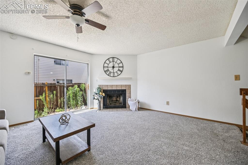 Image 5 of 28: Carpeted living room featuring a tile fireplace, a textured ceiling, and ce