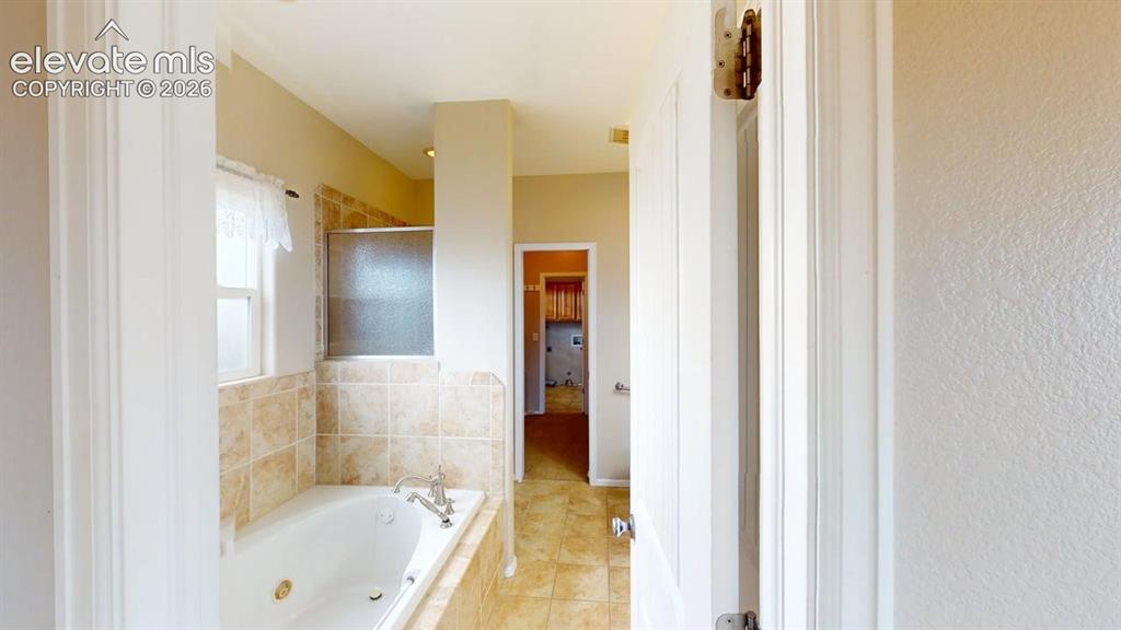 Image 33 of 50: Built-in soaking tub with a tiled surround, an integrated shower with a fro