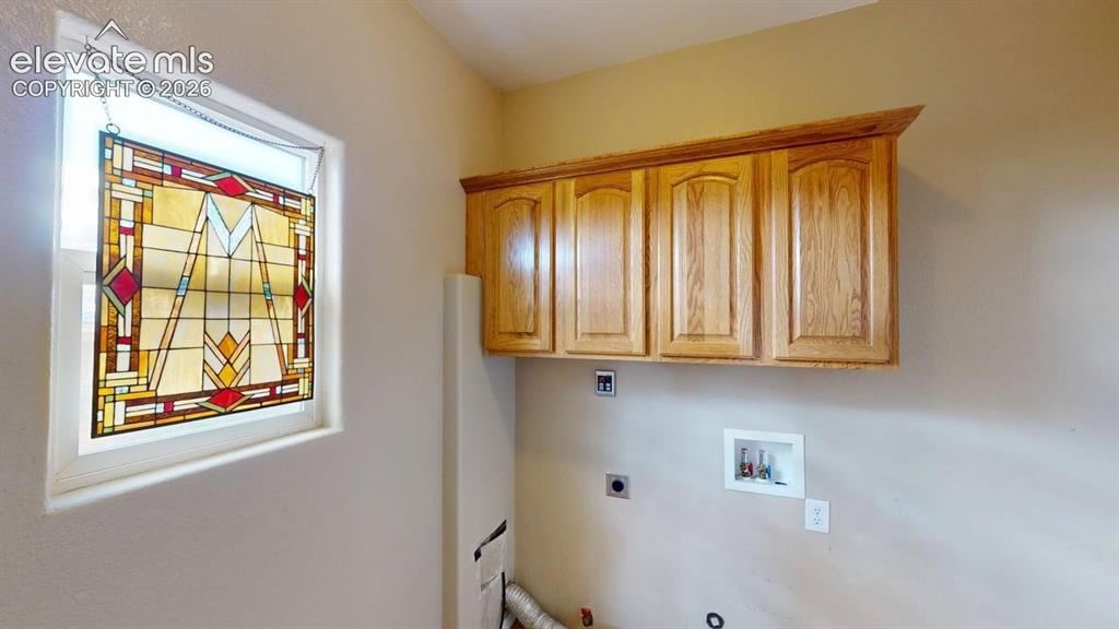 Image 39 of 50: Laundry area featuring wood-finish cabinetry, a framed stained-glass window