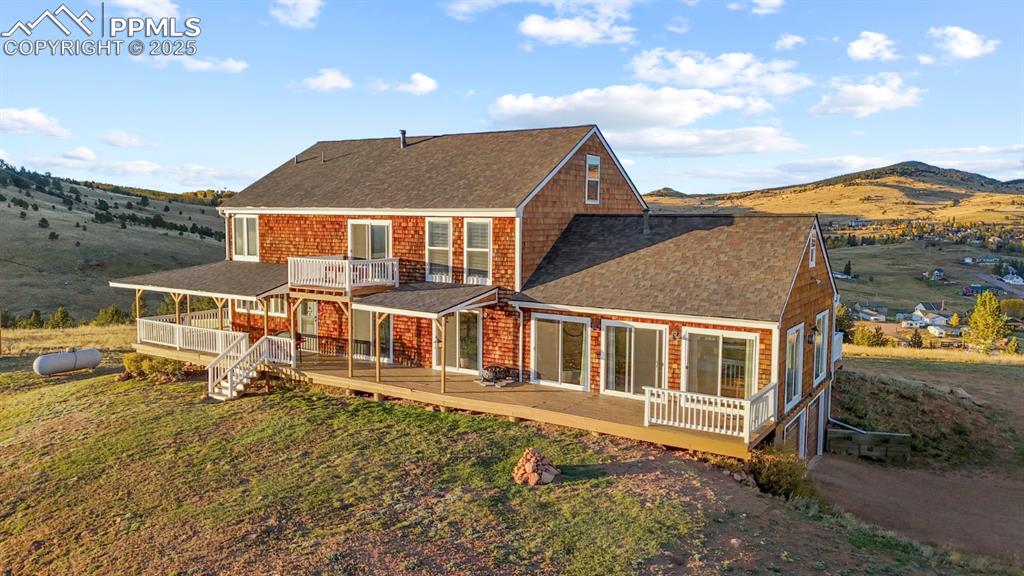 Image 2 of 25: Rear view of house featuring roof with shingles, a wooden deck, and a lawn