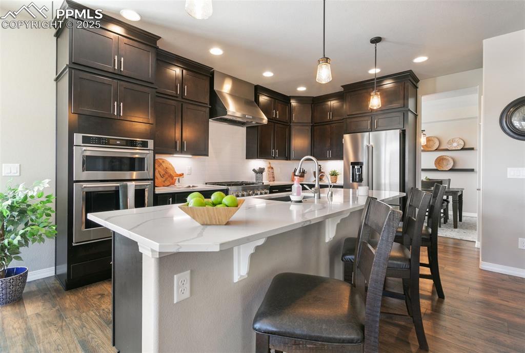 Image 18 of 50: Kitchen with decorative light fixtures, wall chimney range hood, tasteful b