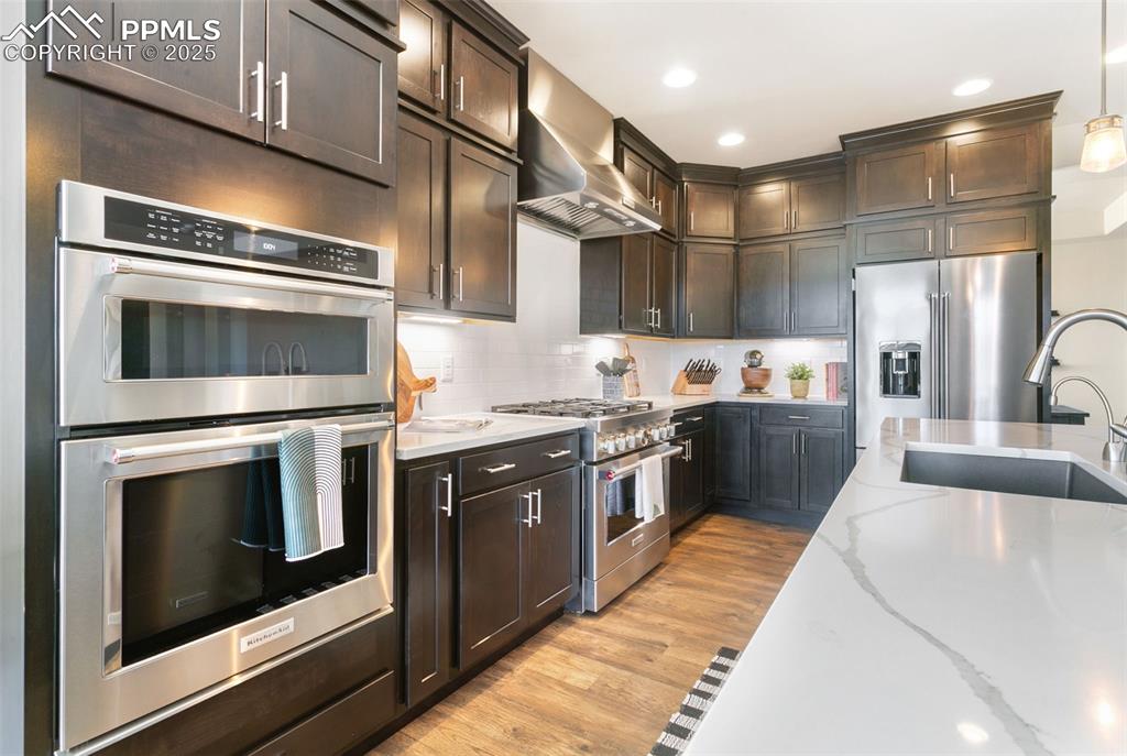 Image 19 of 50: Kitchen featuring premium appliances, wall chimney exhaust hood, light wood