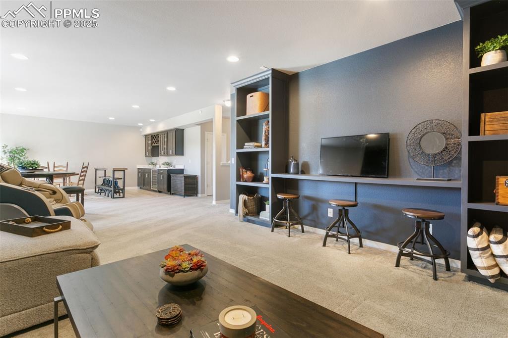 Image 42 of 50: Living room with light colored carpet, recessed lighting, and bar