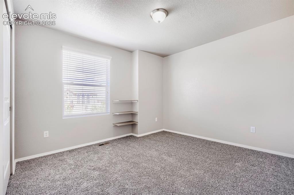 Image 18 of 35: Carpeted room featuring a window with blinds, built-in corner shelving, a f