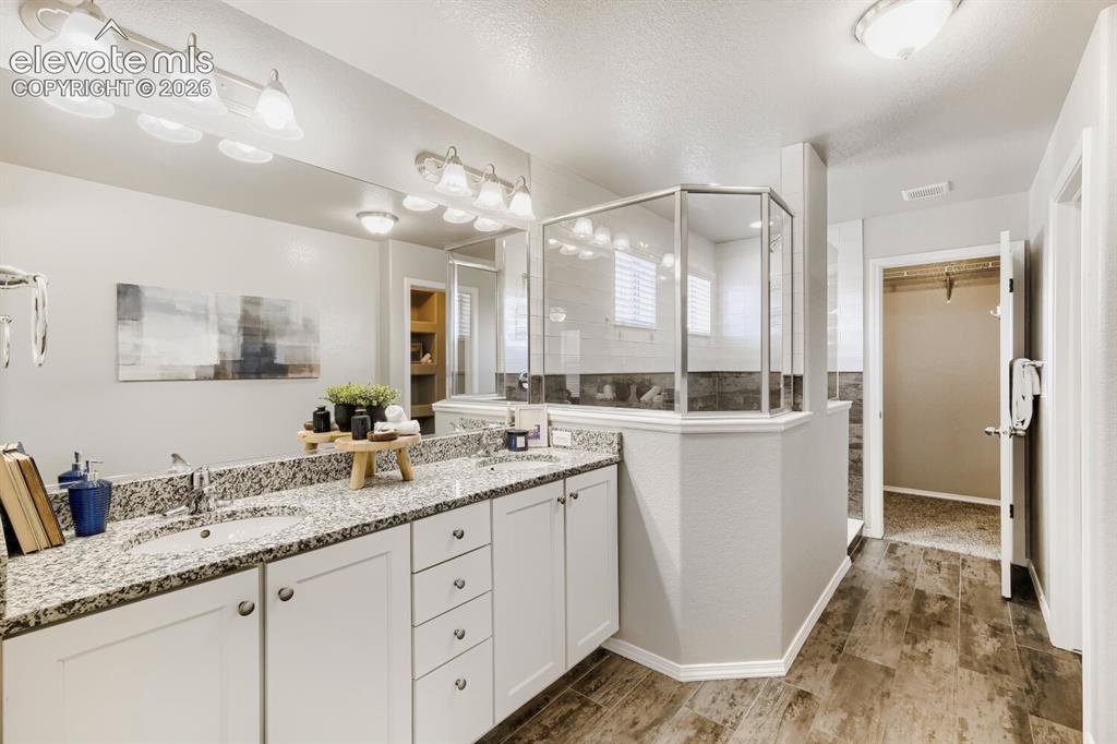 Image 22 of 35: Dual vanity with granite countertops, wood-finish flooring, a glass-enclose