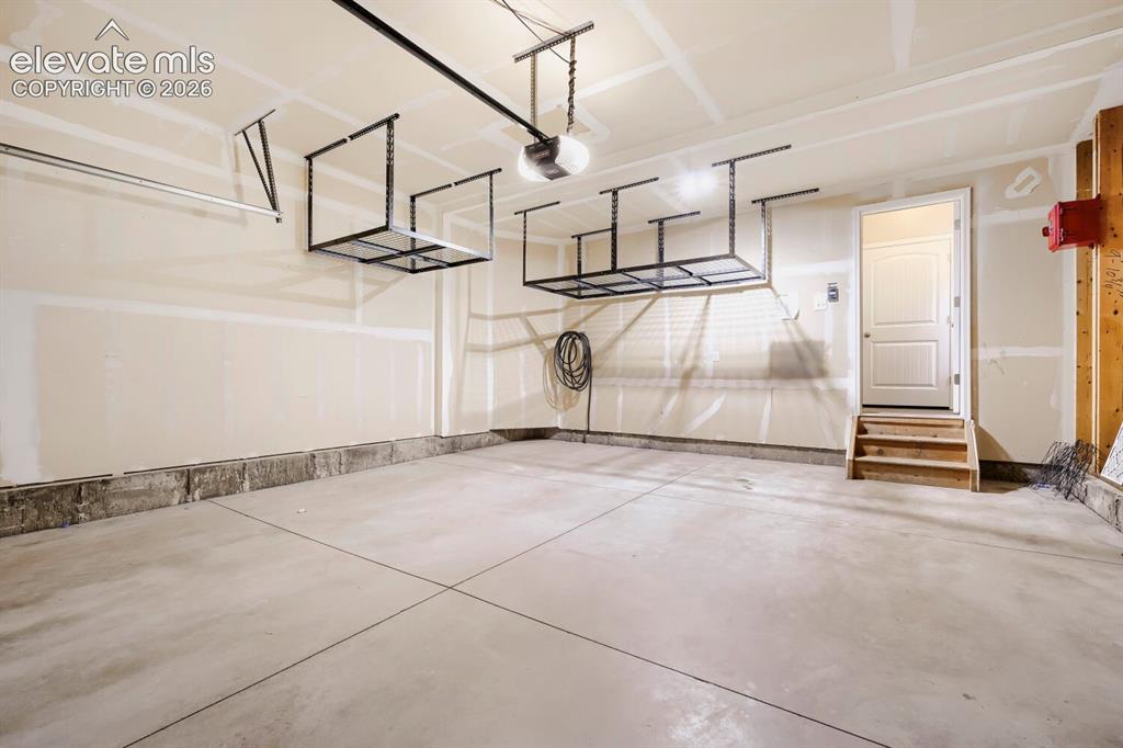 Image 24 of 35: Spacious garage with concrete flooring, overhead storage racks, a single en