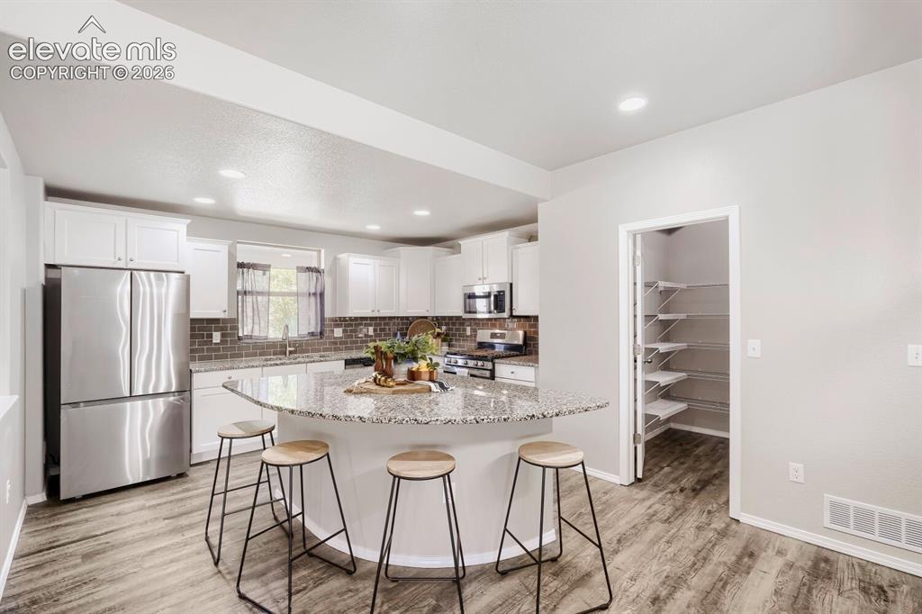 Image 5 of 35: Spacious kitchen featuring an expansive curved island with a stone-finish c
