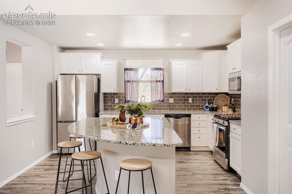 Image 6 of 35: Modern kitchen featuring a large island with granite countertops, white cab