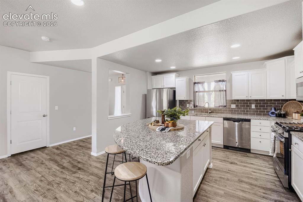Image 7 of 35: Spacious kitchen featuring a large island with a stone countertop, white ca