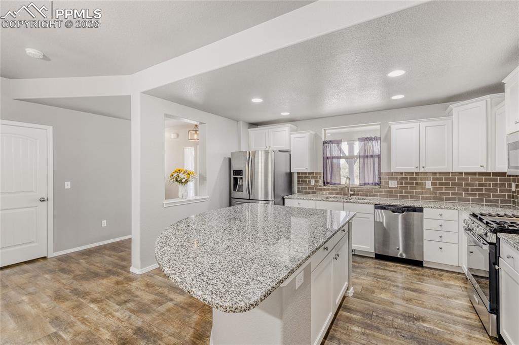 Image 8 of 34: Kitchen with backsplash, white cabinets, stainless steel appliances, LVP fl