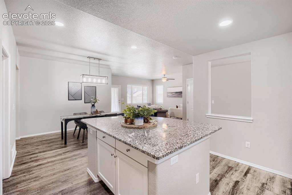 Image 8 of 35: Kitchen island with a speckled countertop, white cabinetry, and recessed li