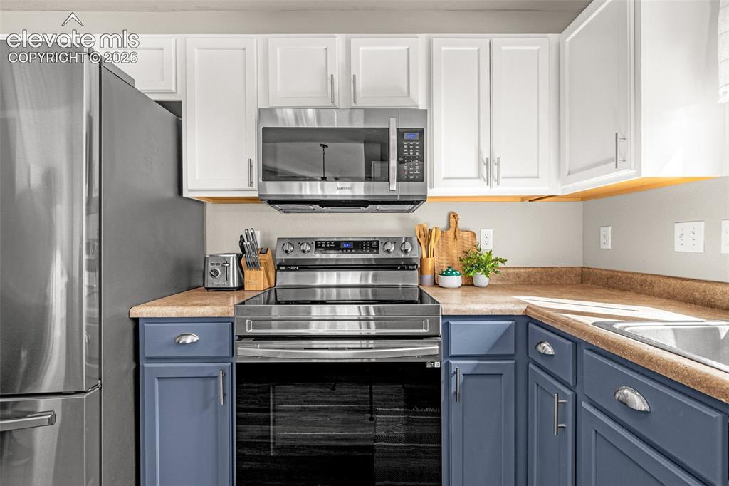 Image 11 of 37: White upper cabinetry, blue lower cabinetry, stainless steel appliances, bu