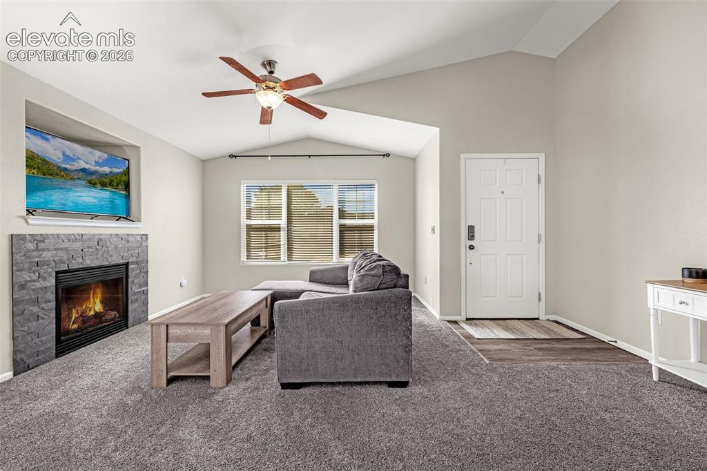 Image 4 of 37: Vaulted ceiling, stone-clad fireplace with mantel, ceiling fan, carpeted fl
