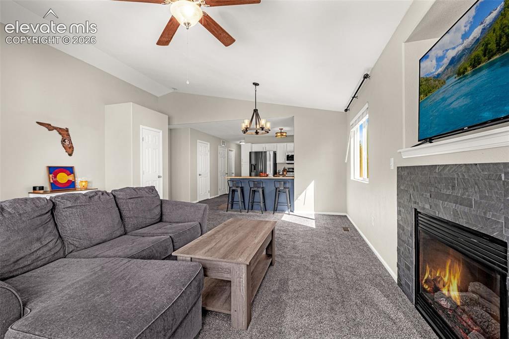 Image 6 of 37: Vaulted ceilings, a ceiling fan, and a fireplace with a stacked stone surro