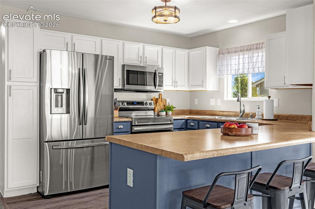 Image 8 of 37: Kitchen featuring stainless steel appliances, white upper cabinetry, blue l
