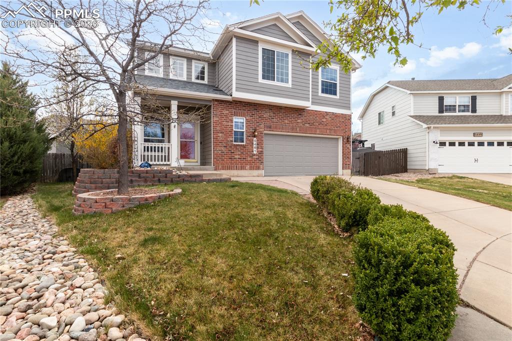 Image 2 of 39: Traditional home with brick siding, covered porch, a garage, and driveway