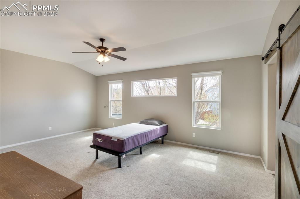 Image 26 of 39: Bedroom with a barn door, light carpet, a ceiling fan, and vaulted ceiling
