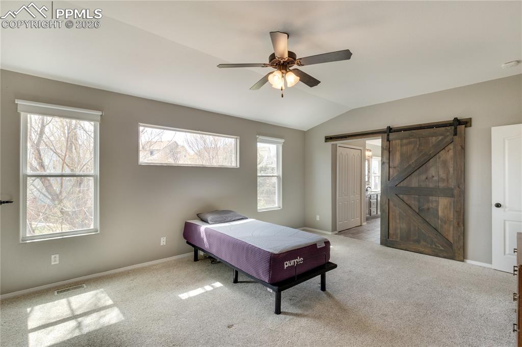 Image 27 of 39: Bedroom featuring a barn door, vaulted ceiling, light carpet, ceiling fan, 