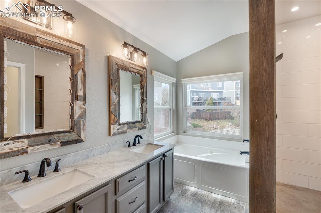 Image 29 of 39: Full bath featuring lofted ceiling, double vanity, and a bath