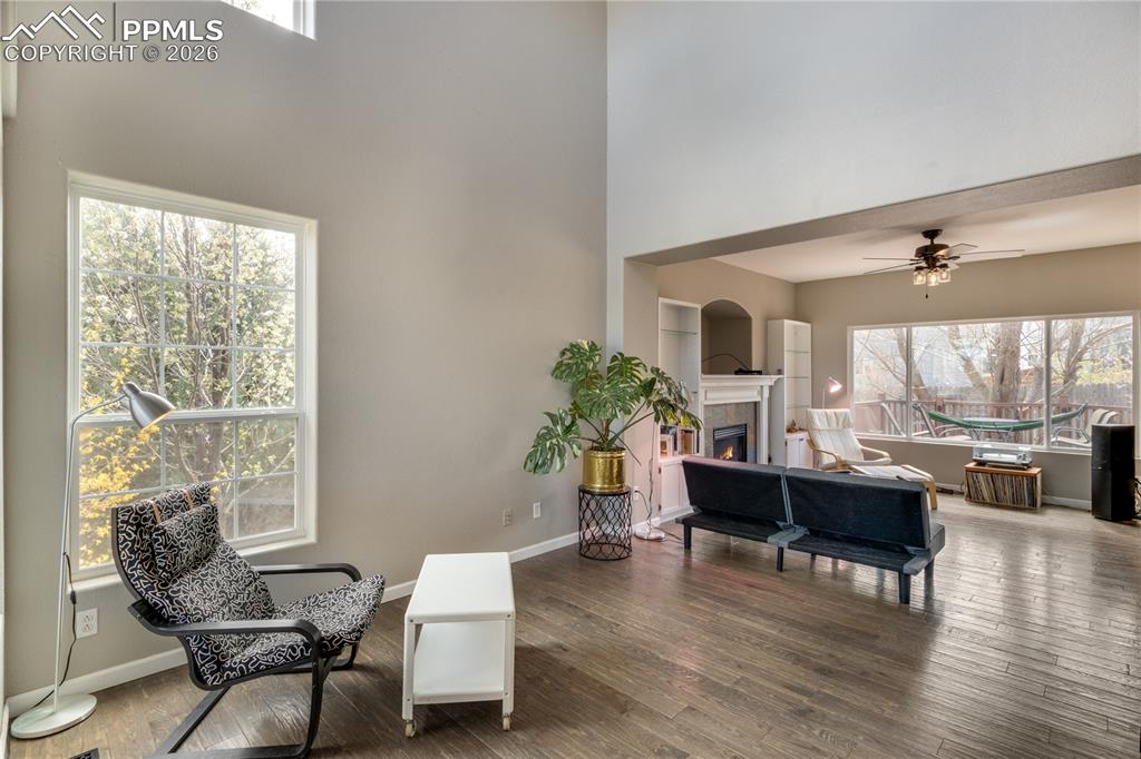 Image 3 of 39: Sitting room with a lit fireplace, a high ceiling, ceiling fan, and wood fi